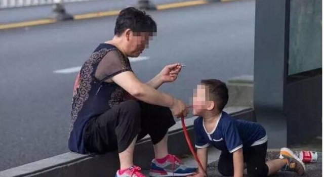 大妈坐街头一边抽烟 一边让孙子学狗爬嘴还叼玩具蛇